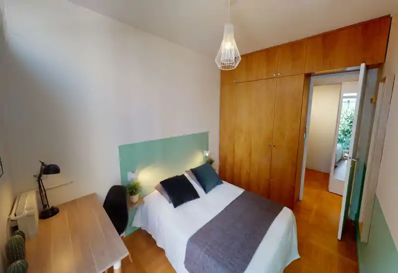 Chambre confortable et lumineuse avec lit double, tête de lit verte, grands placards en bois intégrés et un petit bureau — idéale pour un séjour agréable.