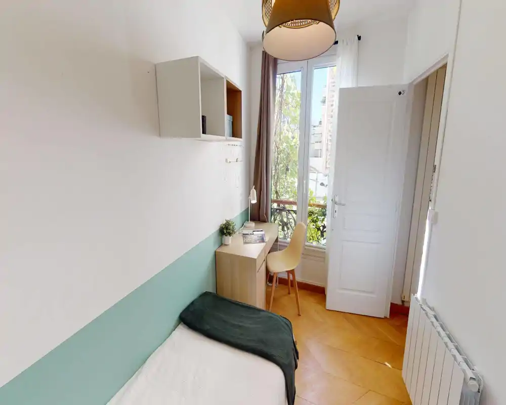 Habitación pequeña y luminosa con cama individual, suelo de parquet, escritorio junto a la ventana y detalles en tonos pastel; ideal para estudiante o persona sola.