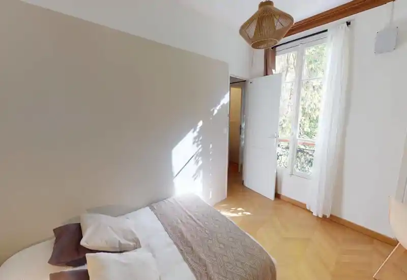 Dormitorio luminoso y aireado con una cama doble cómoda, suelo de parquet en espiga y una gran ventana que aporta mucha luz natural.