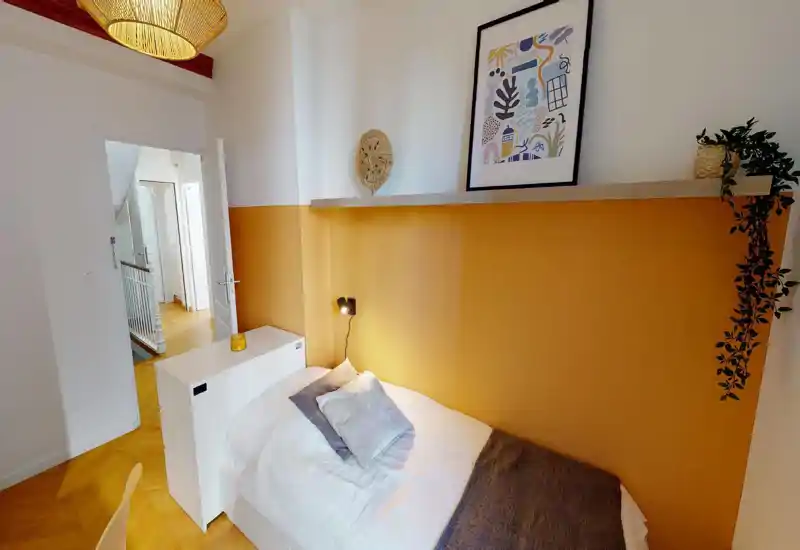 Dormitorio compacto y acogedor con cama individual, pared de acento color ocre y estante decorativo; luz natural y tejidos suaves que lo hacen acogedor.