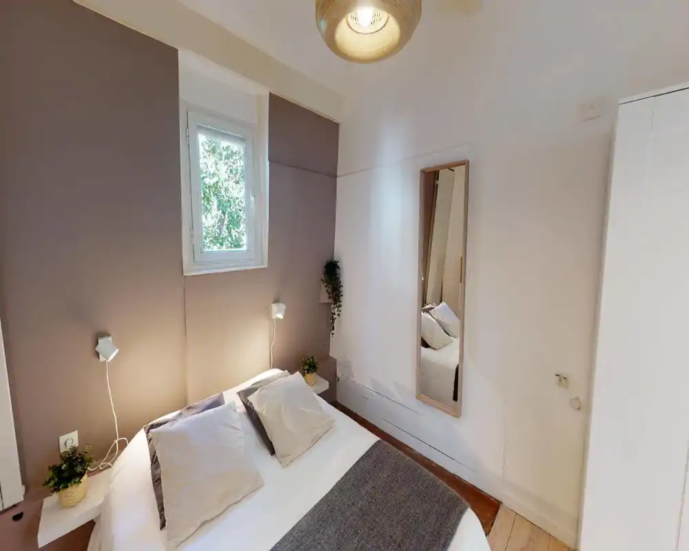 Dormitorio luminoso y acogedor con cama doble, ropa de cama suave, lámparas de mesilla y una pequeña ventana que aporta luz natural.