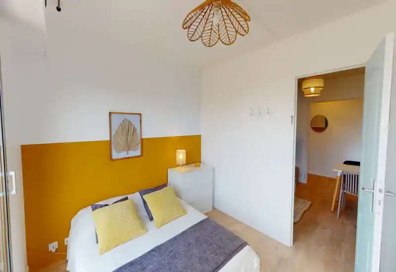 Bright, well-styled bedroom with a double bed, yellow accent wall and coordinating cushions; simple dresser and bedside lamp create a cozy, modern look.