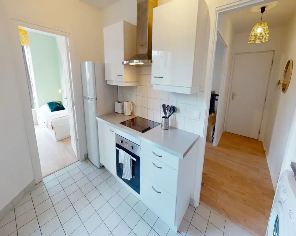 Bright modern kitchen with white cabinets, induction hob, built-in oven and fridge. Clean tiled floor and practical counter space ideal for a compact apartment.