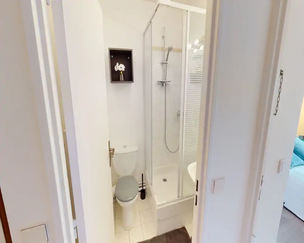 Compact, well-lit bathroom with a corner shower, toilet and tiled floor — ideal for short stays or guest use.