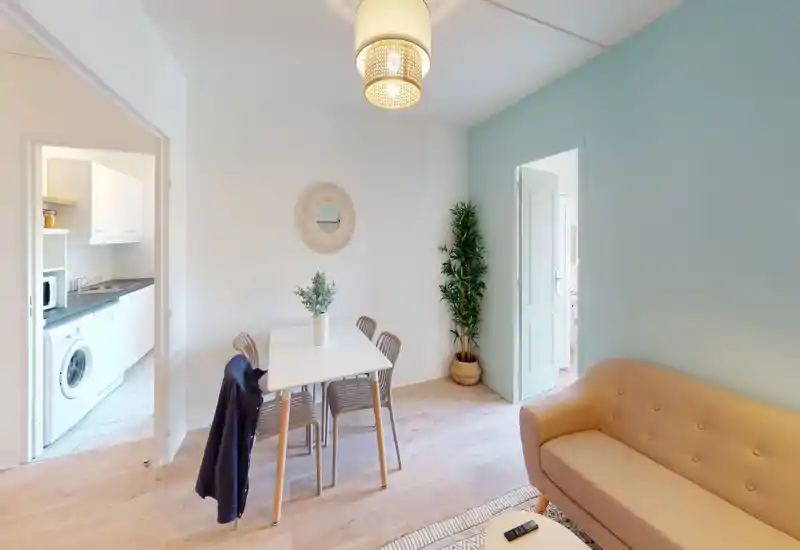 Espace salon lumineux et soigné avec un petit canapé, une table à manger et chaises, une plante décorative et un mur d'accent bleu-vert — un coin chaleureux pour se détendre et dîner.