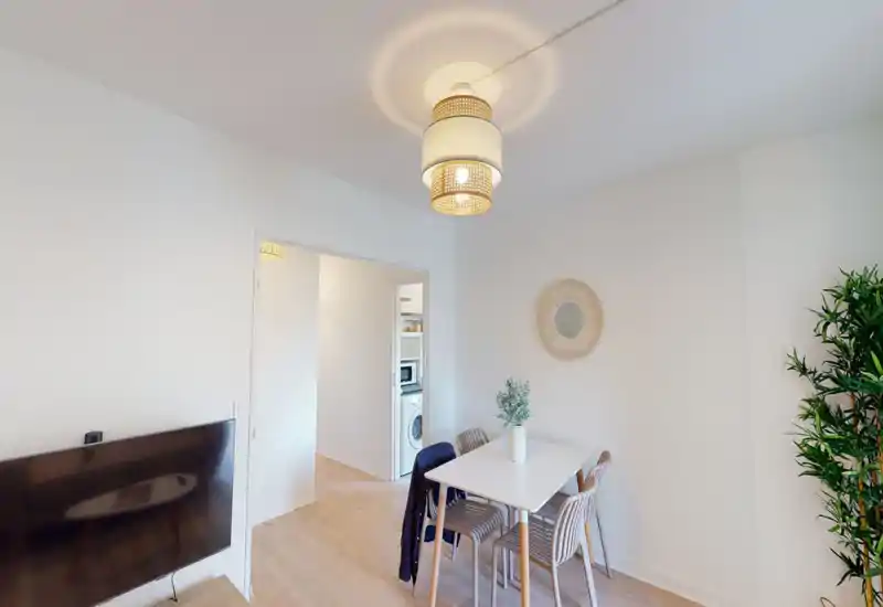 Espace séjour/salle à manger lumineux et moderne avec une table pour quatre, un miroir décoratif et une plante; suspension chaude et TV murale pour un espace polyvalent et convivial.