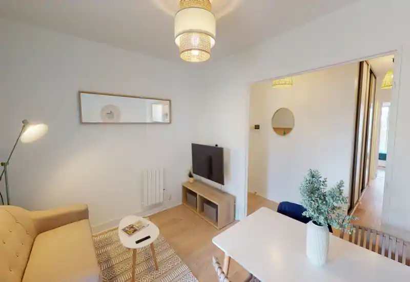Espace de vie lumineux et bien mis en scène avec canapé beige, petite table basse, télévision sur meuble bas et table à manger avec vase — moderne, cosy et épuré.