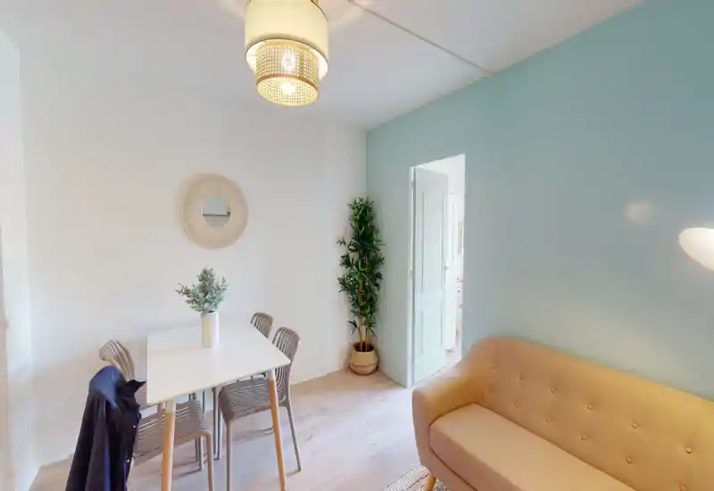 Espace de vie lumineux et moderne avec une petite table à manger, un canapé confortable et des éléments décoratifs légers qui créent une ambiance chaleureuse.