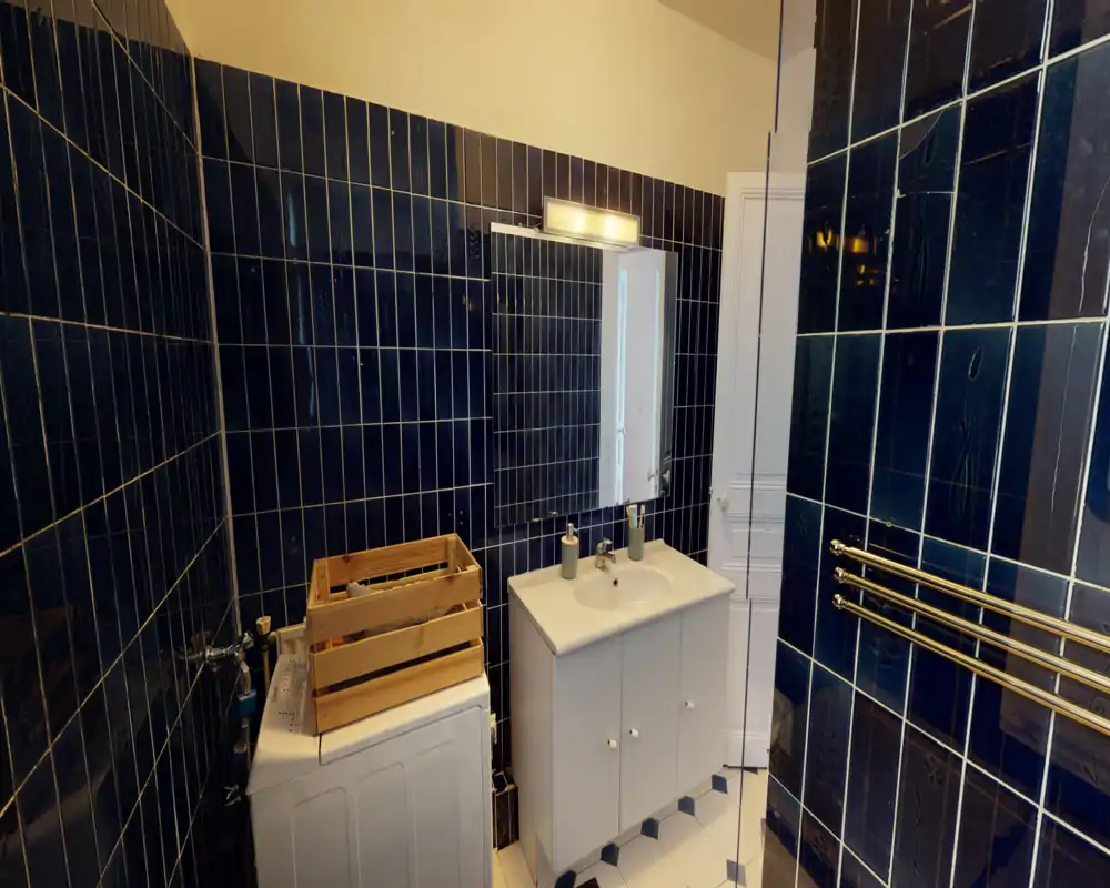 Bagno moderno piastrellato con mobile lavabo bianco, specchio e lavatrice; piastrelle scure verticali e termoarredo cromato per un aspetto contemporaneo.