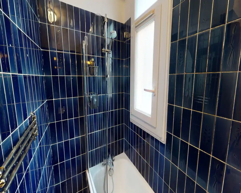 Bagno contemporaneo con pareti piastrellate blu profondo, vasca e doccia a parete accanto a una finestra smerigliata.