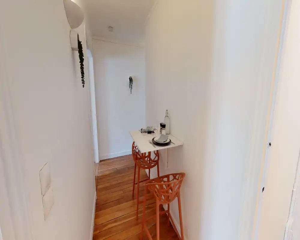 Ingresso/corridoio stretto con un piccolo bancone a muro e due sgabelli arancioni moderni; pareti bianche e pavimento in legno creano uno spazio d’ingresso funzionale e compatto.