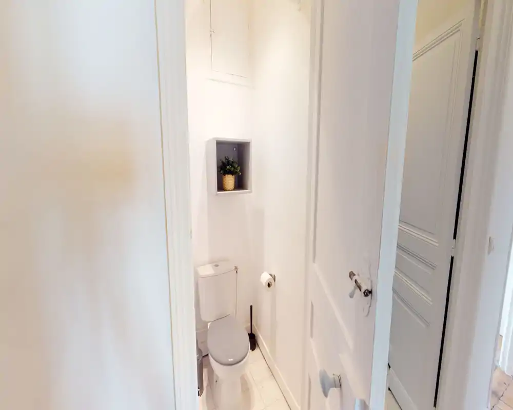 Bagno piccolo e luminoso con wc, nicchia a muro con mensola e piastrelle bianche — compatto e pulito.