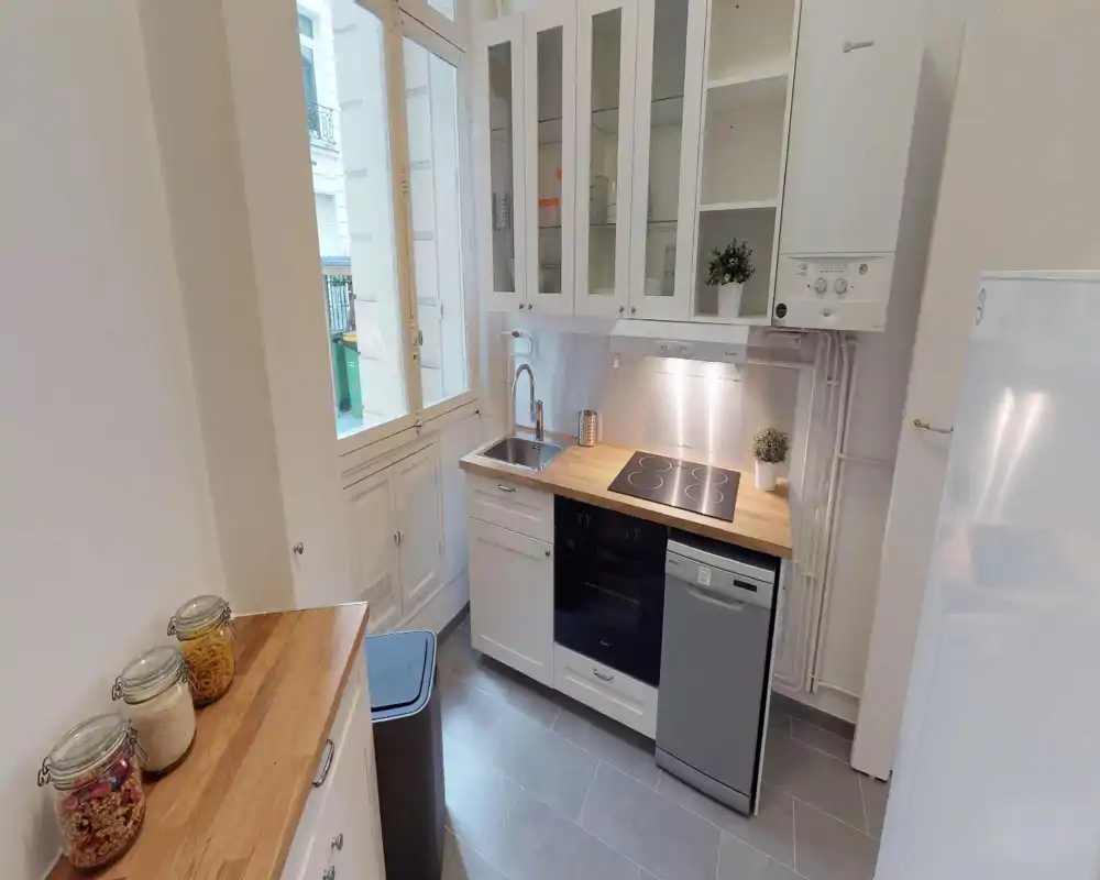 Cucina compatta e luminosa con piano in legno, piano cottura elettrico, forno incassato e lavastoviglie — armadi ordinati e una finestra che garantisce luce naturale.