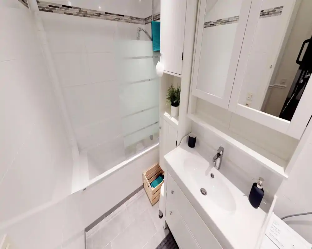 Bagno moderno e pulito con piastrelle bianche, vasca con pannello in vetro smerigliato, lavabo con mobiletto e pensile specchiato — luminoso e ben curato.