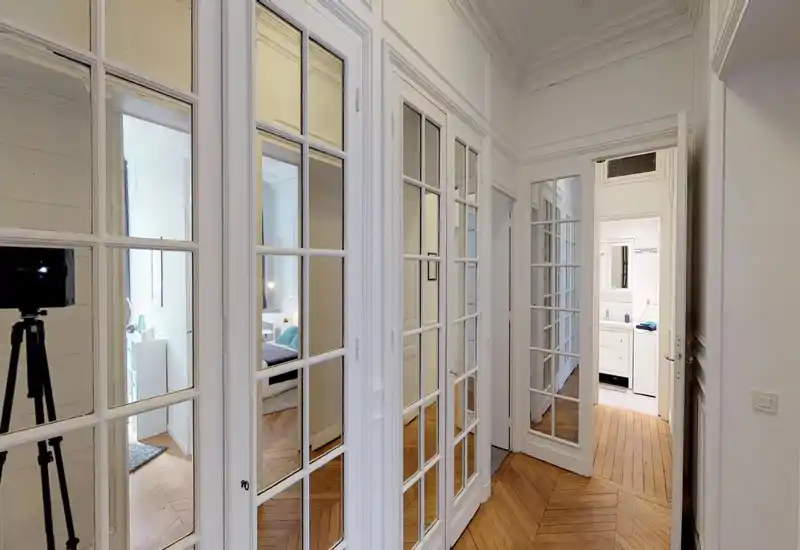 Ingresso/corridoio luminoso ed elegante con boiserie classica e porte a vetri in stile francese che si affacciano sulle stanze adiacenti; pavimento in parquet e luce naturale rendono l'ambiente accogliente.