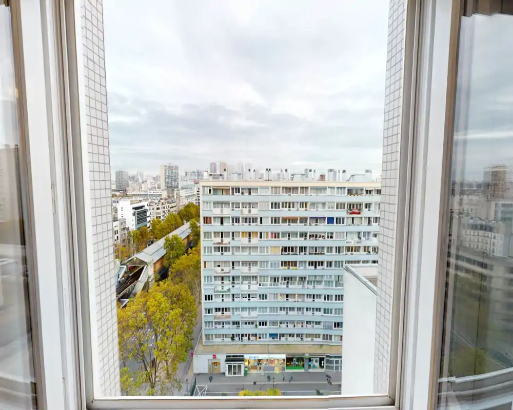 Vista urbana luminosa attraverso una grande finestra che mostra un blocco residenziale e chiome d’alberi — perfetta per valorizzare la posizione e il contesto cittadino.
