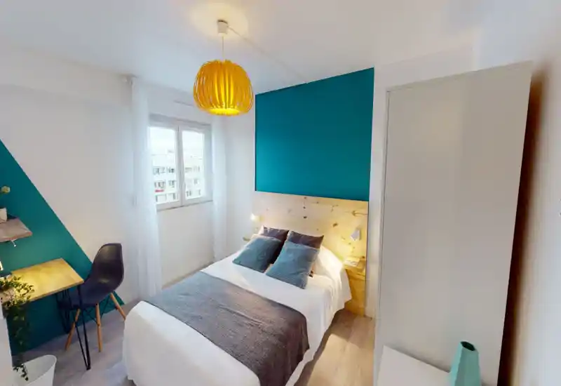 Camera da letto moderna e luminosa con letto matrimoniale ben rifatto, parete accentuata color teal e testiera in legno naturale; la finestra garantisce luce e la lampada a sospensione crea atmosfera.