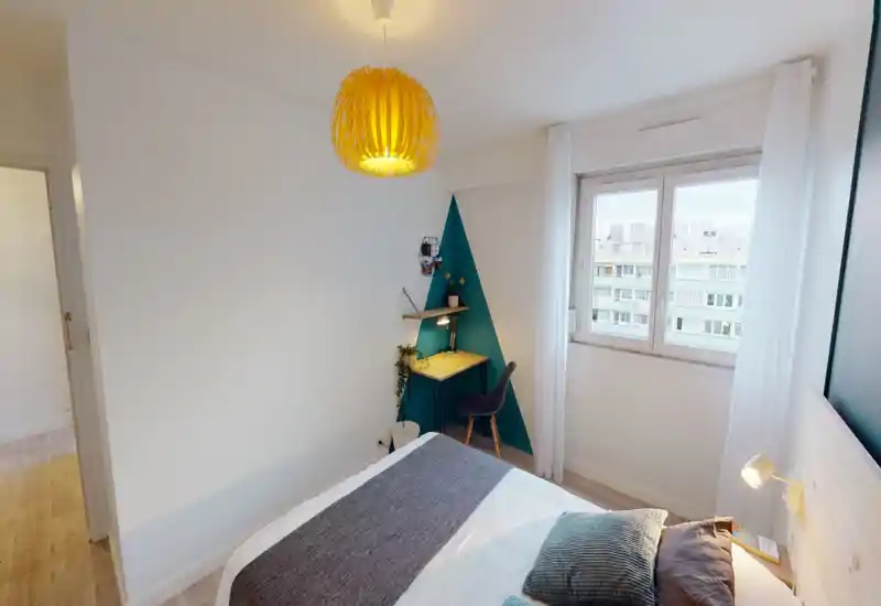 Camera da letto moderna e luminosa con letto ben rifatto, testiera in legno con lampada da comodino e una scrivania compatta davanti a una parete accentuata turchese, perfetta per riposare o lavorare.