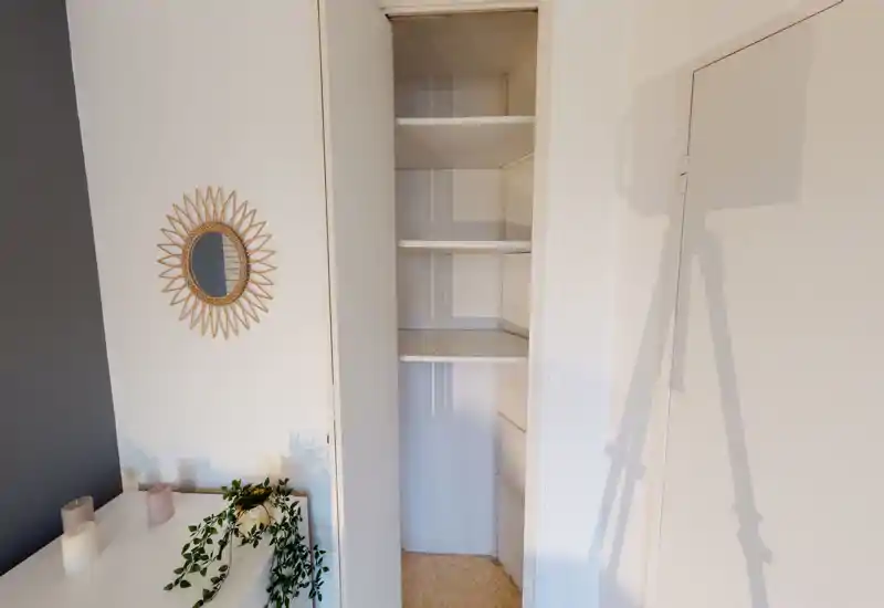 Étagères ouvertes/placard et coin commode décoré avec miroir et plante ; détail d'un espace de vie neutre et bien éclairé mettant en valeur le rangement et la mise en scène.