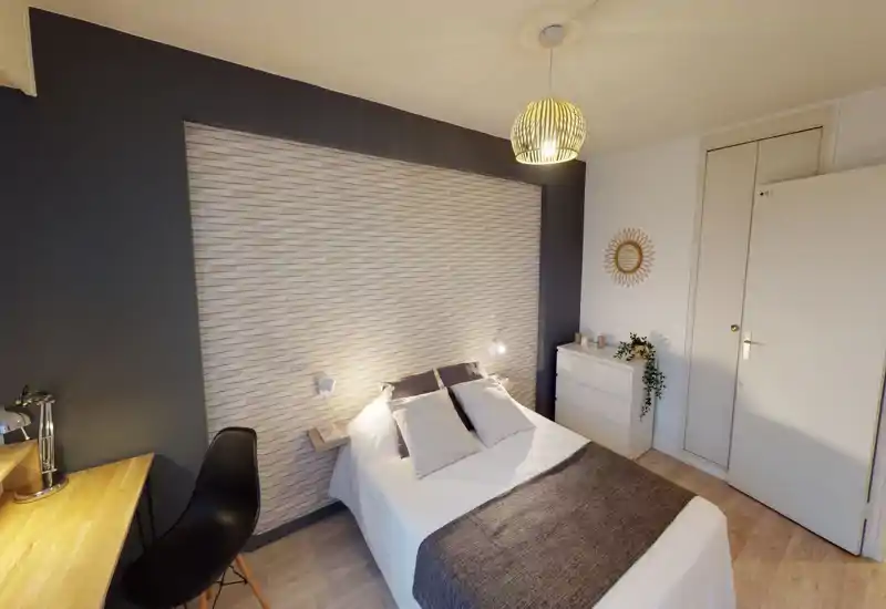 Chambre claire et soignée avec lit double centré devant un mur texturé, lampes de chevet et commode bien rangée — chaleureuse et bien éclairée.