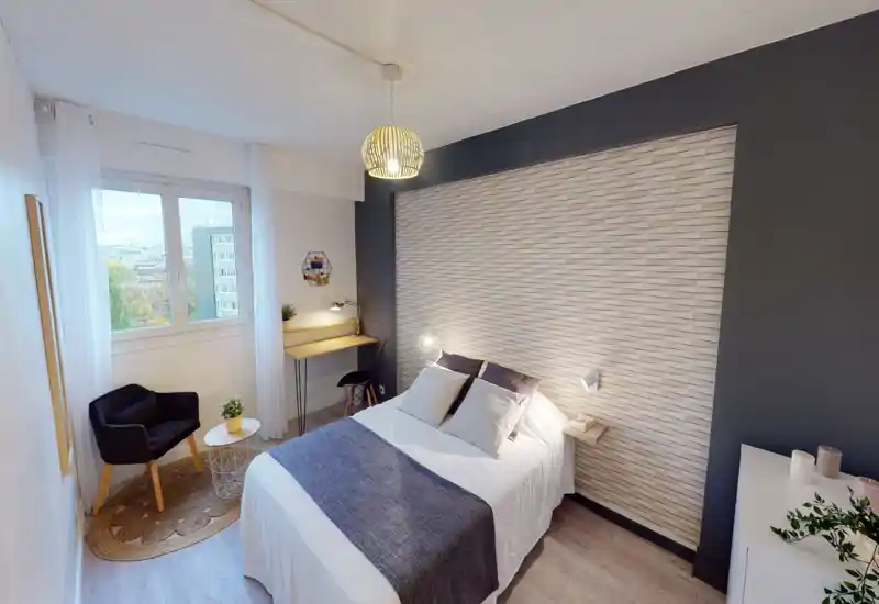 Chambre lumineuse et élégante avec lit double confortable, mur texturé et petit bureau près de la fenêtre — idéale pour se reposer ou télétravailler.