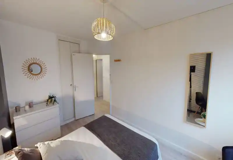 Chambre lumineuse et soignée avec un grand lit bien fait au premier plan, commode blanche, miroir décoratif et suspension apportant une ambiance moderne et chaleureuse.