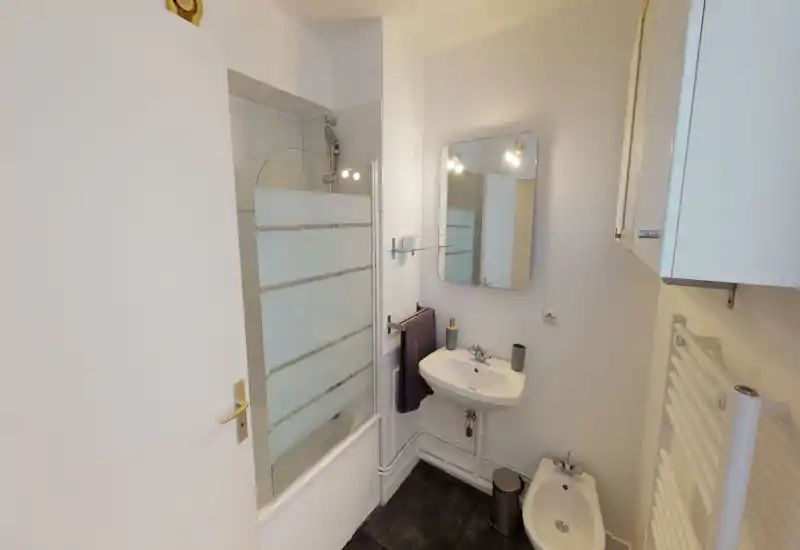 Compact, modern bathroom with a bathtub/shower combination, wall-mounted sink, bidet and mirror; clean white finishes and practical accessories.