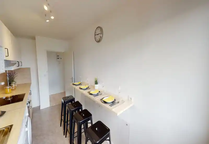 Modern galley kitchen with a light wood countertop, built-in appliances and a breakfast bar with stools set for four — bright and neatly staged for guests.