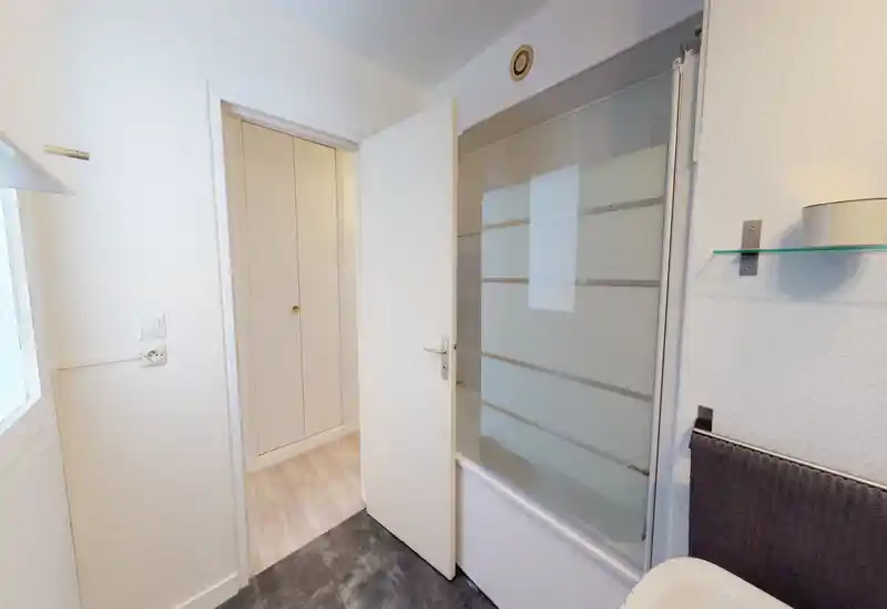 Small bright bathroom with a glass shower screen, white door and modern fixtures. Clean, neutral finishes and a towel rail visible next to the sink.
