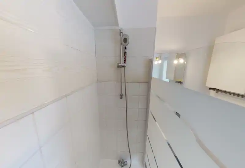 Compact, well-lit shower area with white tiles, a chrome handheld shower head and frosted glass partition; clean neutral design suitable for rental listings.