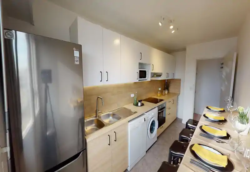 Modern fully equipped kitchen with wood-effect countertops and backsplash, stainless fridge, built-in oven, dishwasher and washing machine; breakfast bar set with plates and glasses.