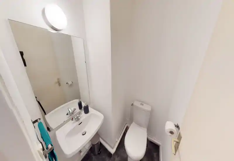 Compact, well-lit bathroom with a wall-mounted sink, mirror, and a close-coupled toilet — simple and functional for a rental.