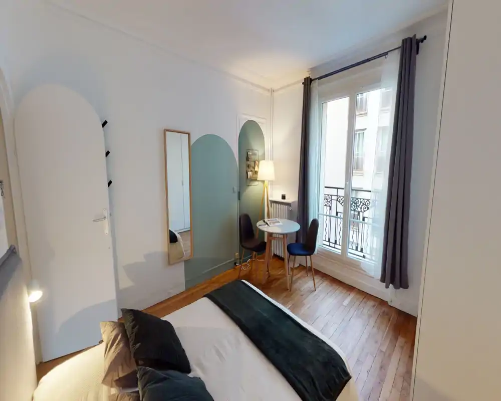 Chambre lumineuse et élégante avec un grand lit confortable, des textiles chaleureux et un coin table près d'une grande fenêtre donnant sur un balconnet.