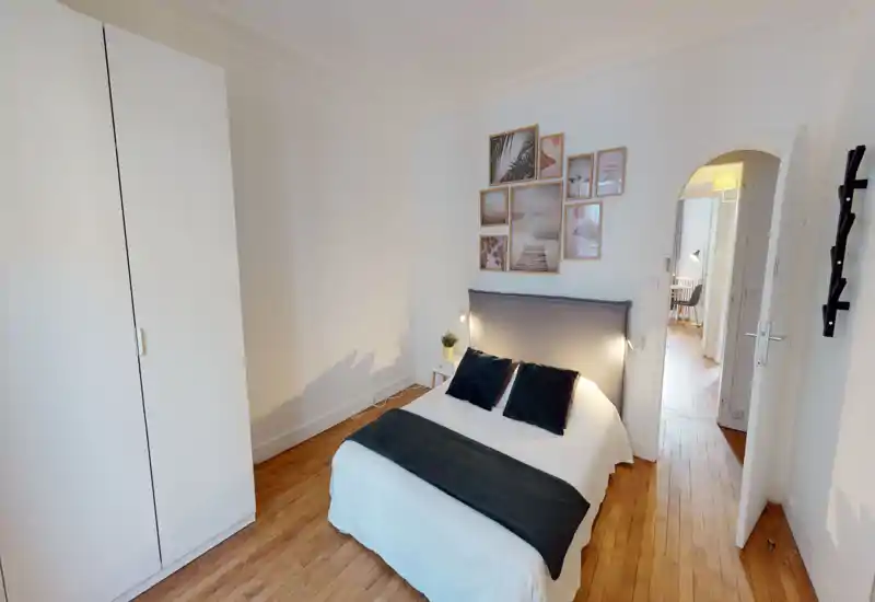 Bright, stylish bedroom with a comfortable double bed, grey upholstered headboard, decorative pillows and framed wall art; hardwood floors and soft lighting create a welcoming atmosphere.
