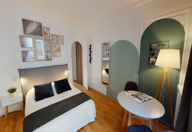 Bright, stylish bedroom with a comfortable double bed, decorative wall gallery and a small dining/desk corner with a floor lamp — ideal for a cozy stay.