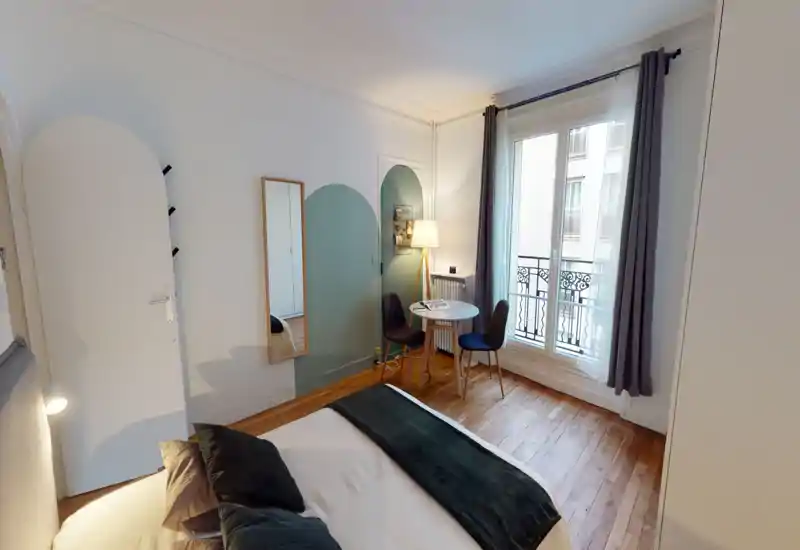 Well-lit, stylish bedroom with a comfortable double bed, cozy textiles and a small seating area by a large window leading to a Juliet balcony.