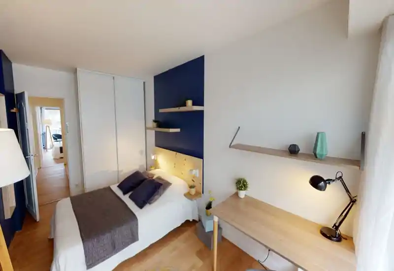 Well-lit bedroom with a double bed against a wooden headboard, floating shelves and a neat desk next to the window — modern, cozy styling ideal for short-term rentals.