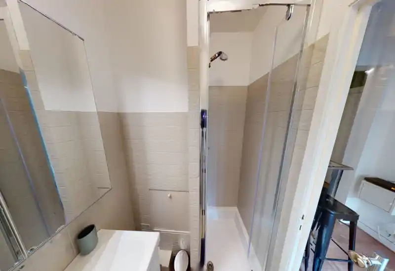 Compact bathroom with a shower cubicle, tiled walls and a small sink with mirror. The space is clean, well-lit and suitable for a rental listing.