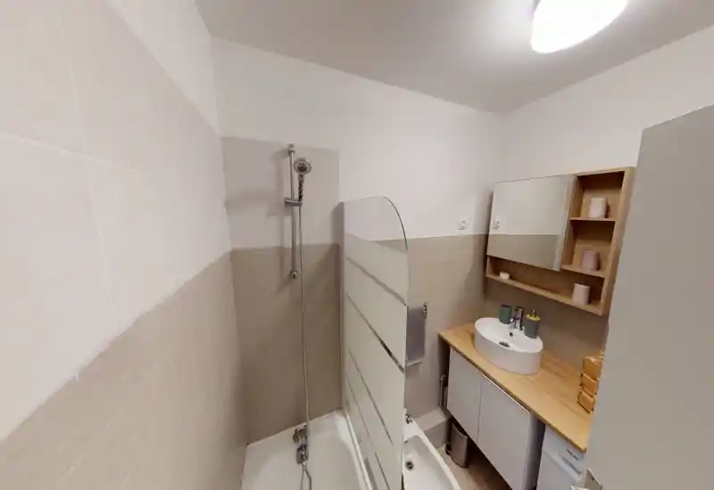 Compact modern bathroom with a shower-bath combination, glass divider, wall-mounted shower head, wooden countertop with vessel sink and mirrored cabinet — bright neutral tones and clean, functional layout.