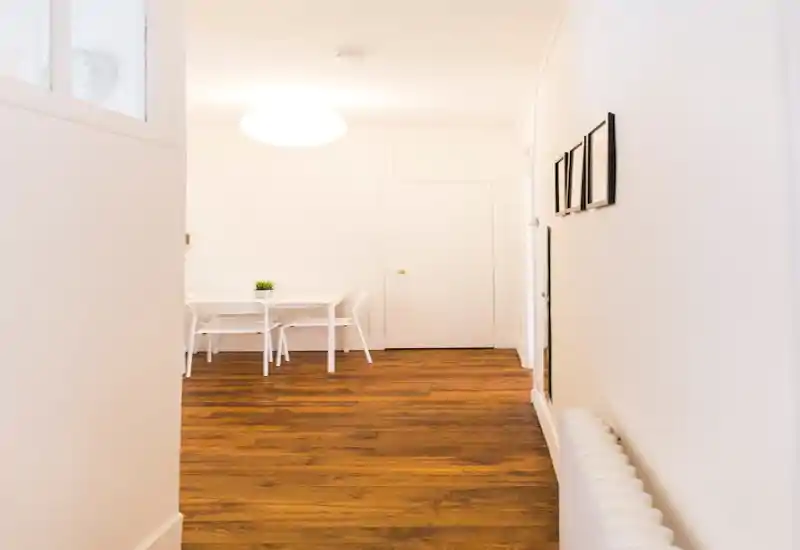 Coin repas lumineux et minimaliste avec petite table blanche, chaises et plante décorative sur un parquet chaleureux — ambiance aérée et sobre, idéale pour la location courte durée.