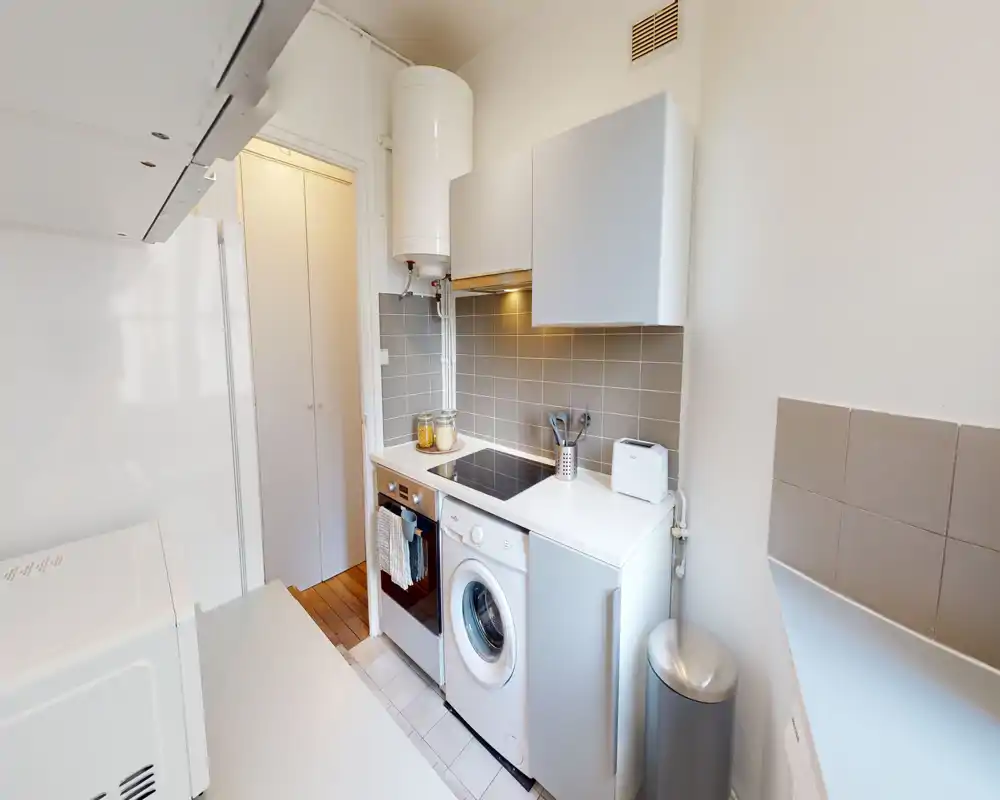 Kitchenette moderne et compacte avec appareils intégrés, plaque à induction, lave-linge et rangements pratiques — lumineuse et bien organisée pour un mode de vie urbain efficace.