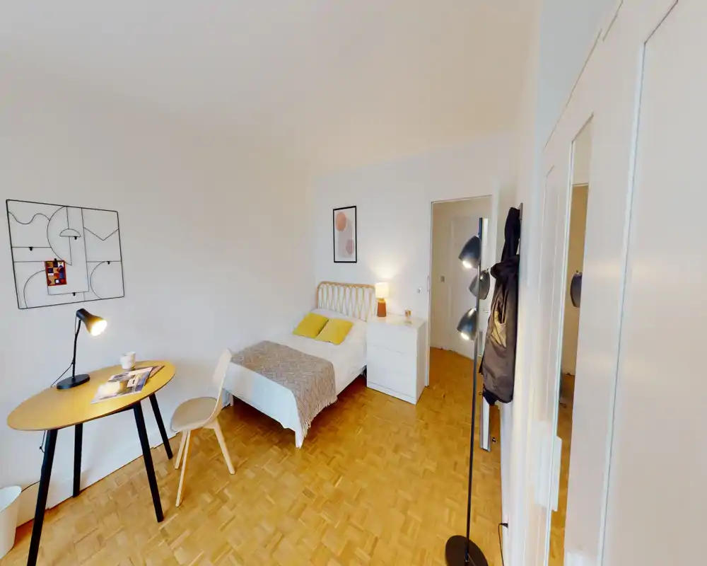Camera da letto luminosa e ordinata con letto singolo, comò e un piccolo angolo studio — ideale per un soggiorno confortevole. Pavimento in parquet caldo, arredo minimale moderno e ottima luce naturale/ambientale.