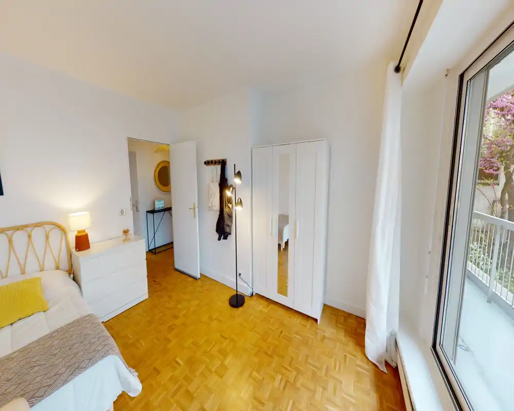 Camera da letto luminosa e ben arredata con letto comodo, armadio bianco con anta a specchio, pavimento in parquet e una grande finestra che illumina la stanza.