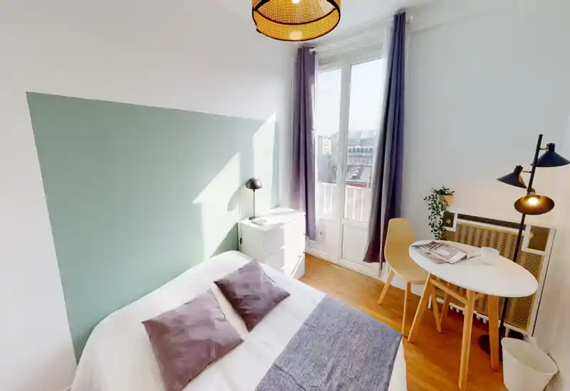 Chambre lumineuse et stylée avec un lit double, coussins moelleux et une petite table près d'une grande fenêtre offrant une vue sur la ville.