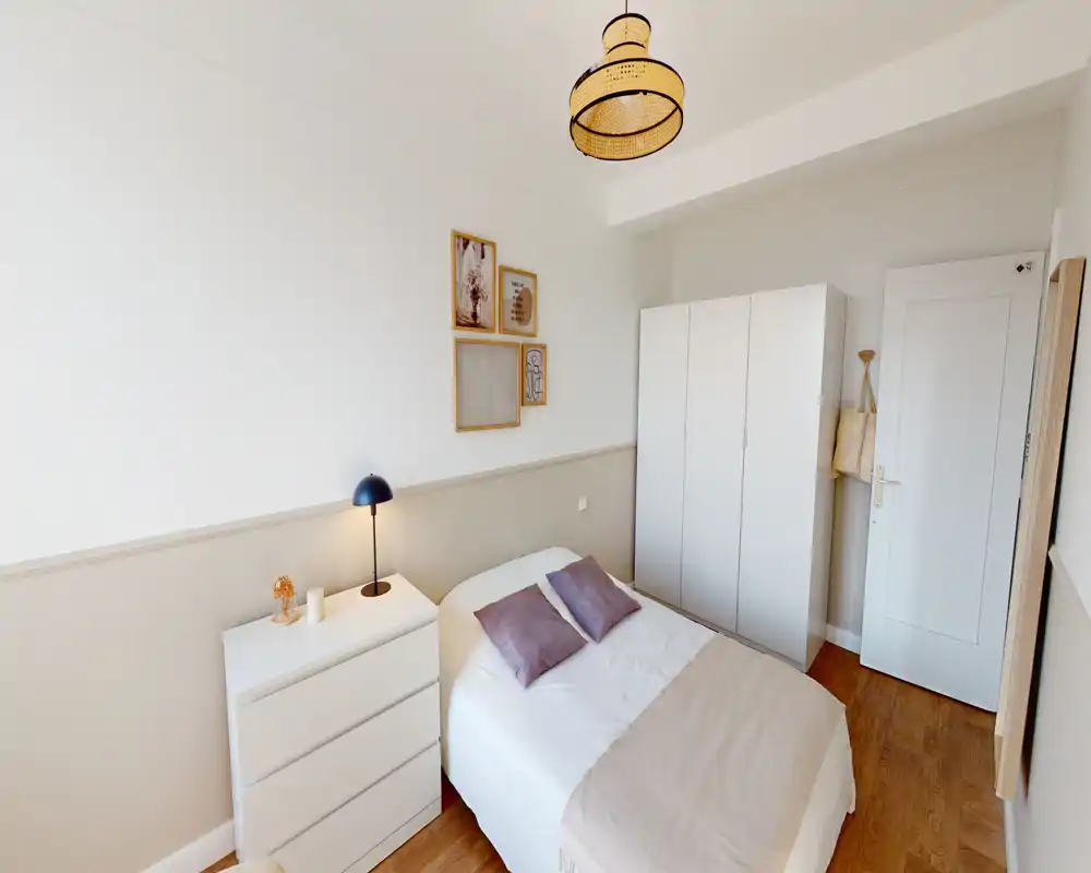 Chambre lumineuse et bien agencée avec un lit double, lampe de chevet, commode et armoire; tons neutres et textiles doux pour une atmosphère apaisante.