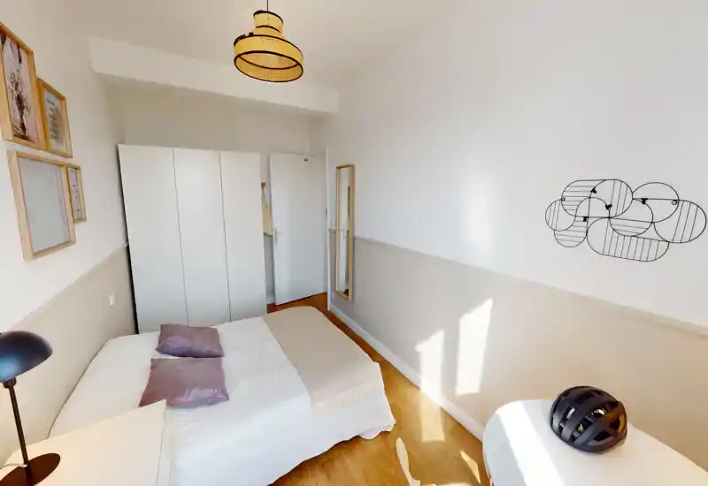 Sunny, compact bedroom with a double bed, soft linens and a white wardrobe; warm wood floors and simple wall decor create a calm, modern feel.
