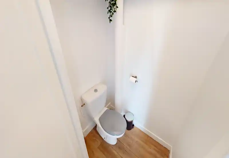Compact, well-lit toilet room with white walls, wood-effect flooring and a modern close-coupled toilet; simple, clean and ready for use.