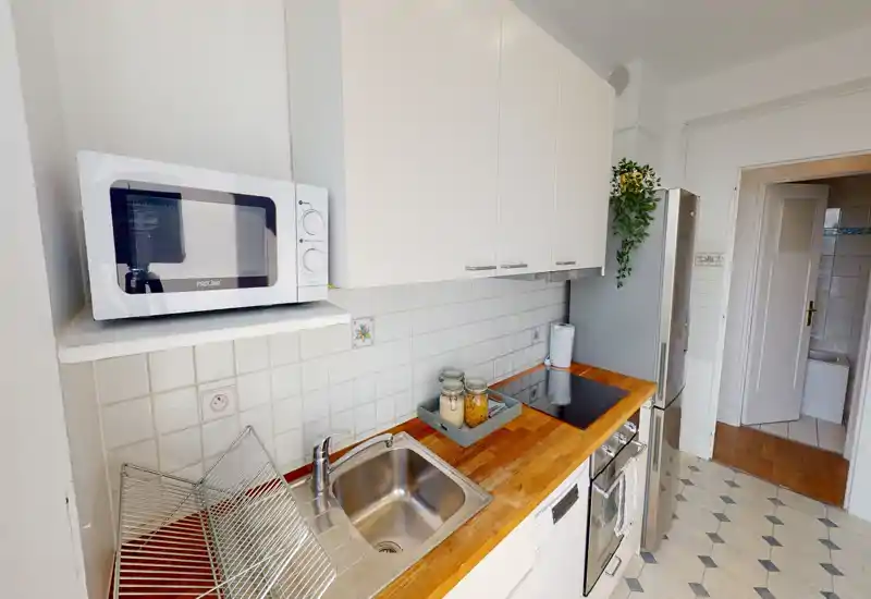 Compact, well-equipped kitchen with wooden countertop, stainless sink, induction hob and a tall fridge; bright, tidy and practical for everyday use.