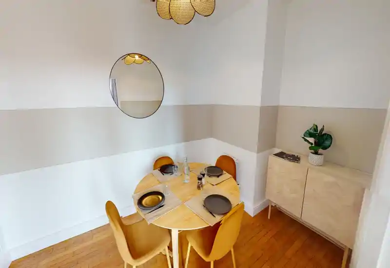 Cozy, styled dining nook with a round wooden table set for four and mustard upholstered chairs, complemented by a sideboard and decorative mirror.