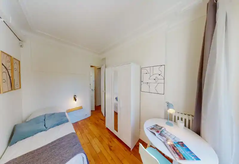 Bright, well-staged single bedroom with wooden floors, a comfortable bed with blue cushions, a white wardrobe with mirror doors and a small workspace by the window.
